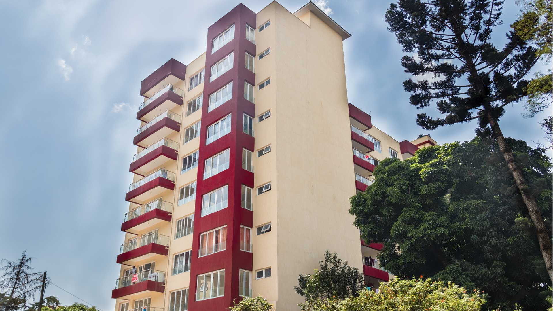 Cream apartment tower at Parklands Square, Nairobi, with a maroon column of windows, glass-railed balconies and a tall pine